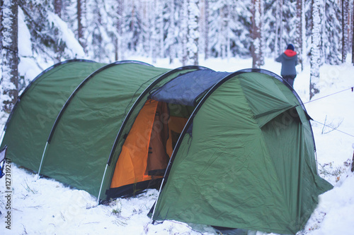 A process of camping in winter forest, setting a tent covered in snow, making a bonfire campfire and cooking food with portable gas cooker and fire, snowy landscape 