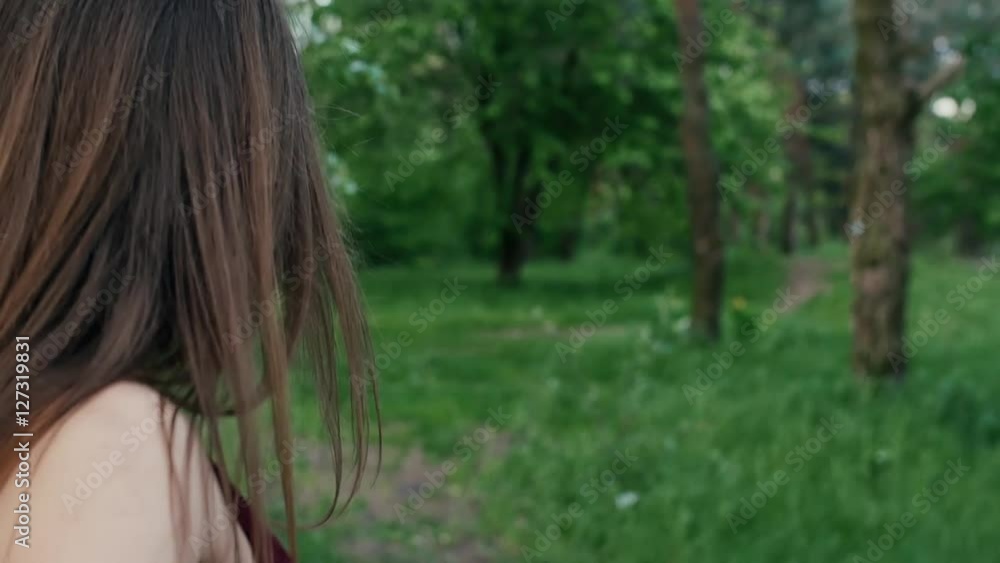 Back view of brunette girl with long hair walking in garden or forest, touching leaves of trees. Slow mo, steadicam shot Back view of brunette girl with long hair walking in garden or forest, touching leaves of trees. Slow mo, steadicam shot