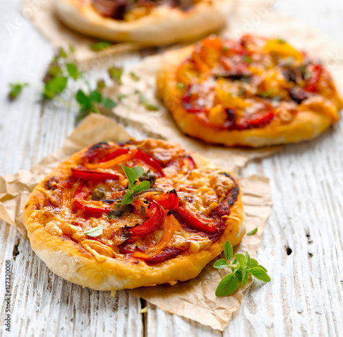 Small homemade vegetable pizza with addition of grilled pepper, tomatoes, cheese and herbs  on a white wooden table