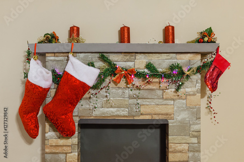 Mantelpiece decorated with Christmas candles, socks, pine tree branches, garland and ribbons above fireplace.
