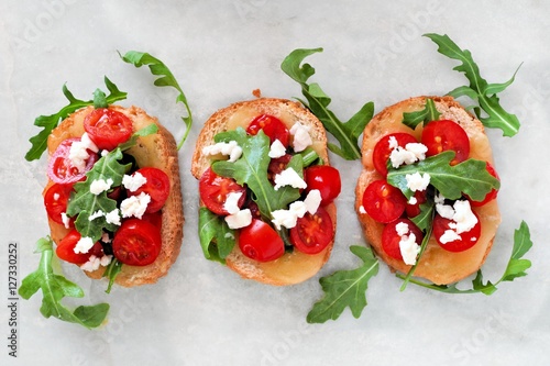 Fotobehang Crostini appetizers with cherry tomatoes, arugula, and cheese, above view on whi