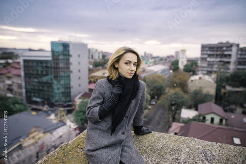 Young attractive woman with good mood enjoying beautiful city landscape while standing on a roof of building, charming smiling hipster girl relaxing after excursion during her amazing spring weekend