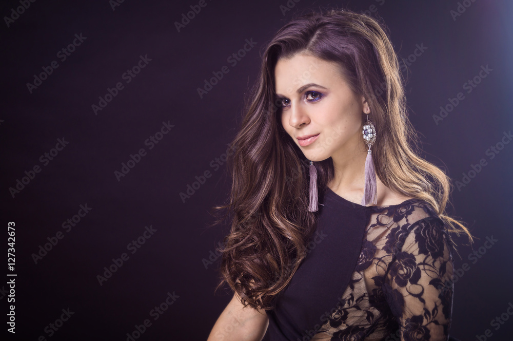 Beautiful brunette girl with flowing hair on a dark background and in earrings Beautiful brunette girl with flowing hair on a dark background and in earrings