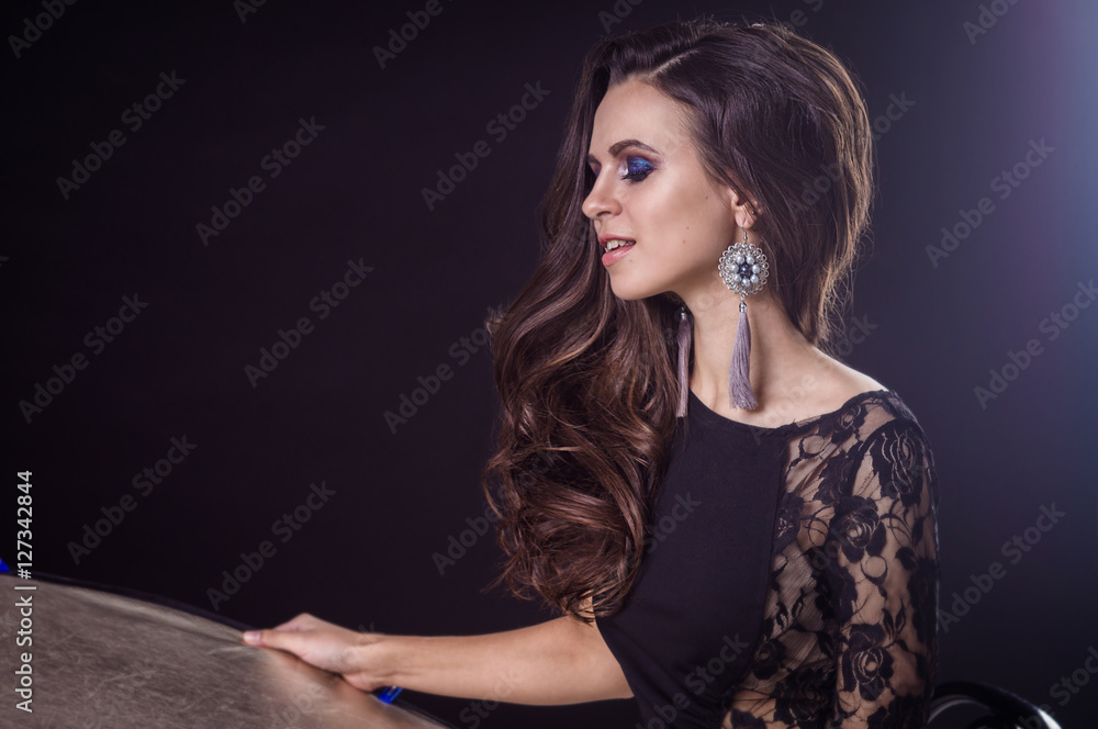Fototapeta premium Beautiful brunette girl with flowing hair on a dark background and in earrings