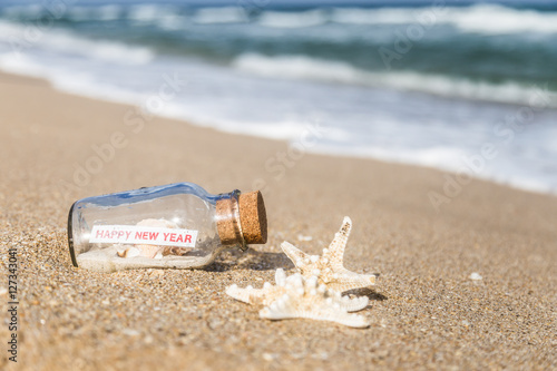 message in a bottle and starfish/bottle with a message happy new year on sandy beach in Florida.