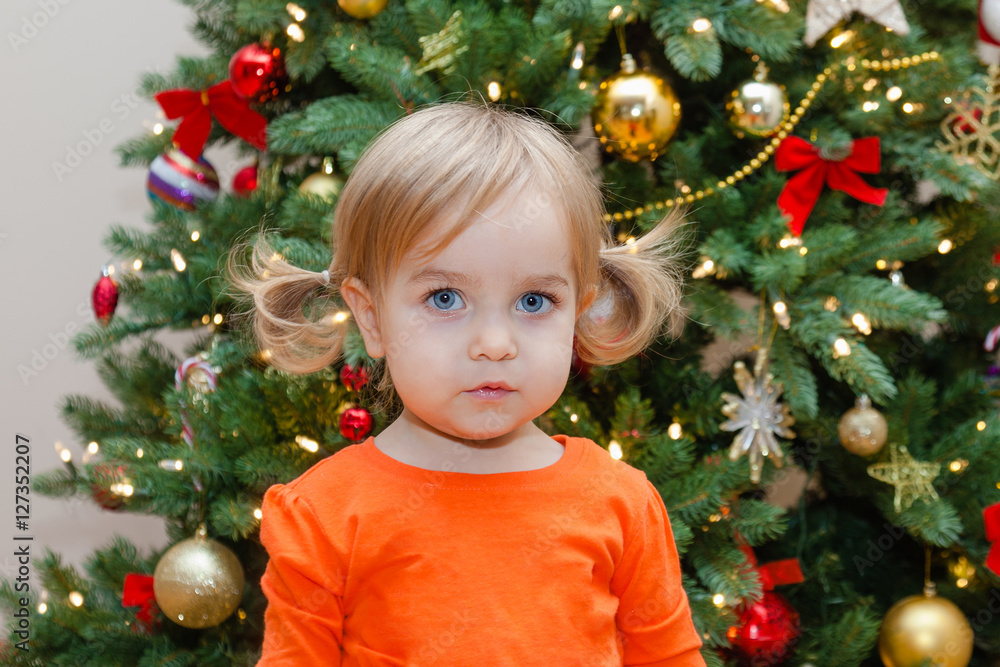 Toddler girl on the Christmas tree background. Child in holiday decorated living room.