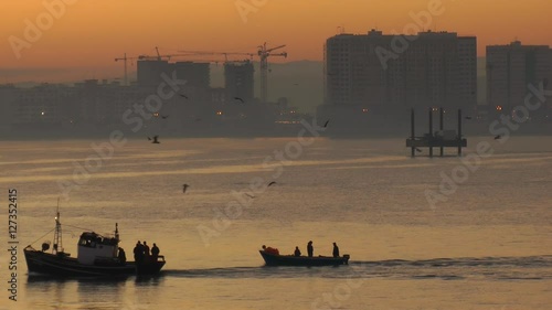 silhouette of a small boat travelling on the water with urban tangier city skyline in the background.