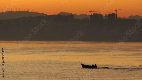 silhouette of a small boat travelling on the water with urban tangier city skyline in the background