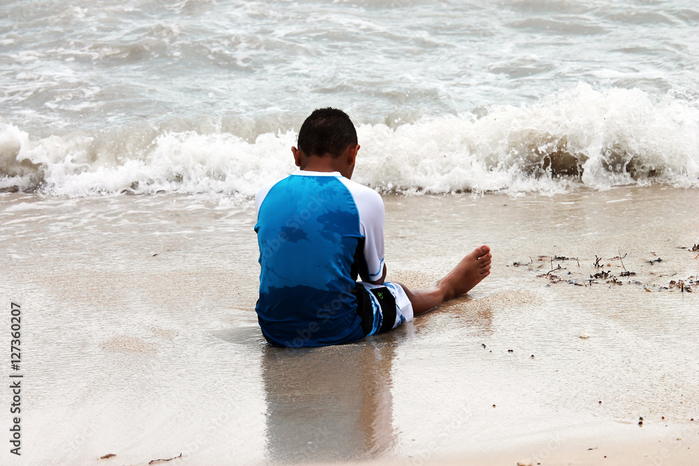 Young Boy Sitting Down Tired on the Beach