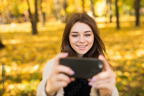 Smile girl taking selfie on mobile phone in sunny autumn park