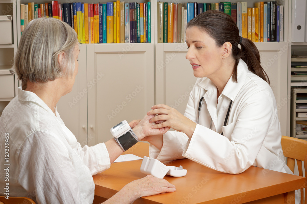 Middle aged doctor explaining the correct use of a wrist blood pressure meter to her senior female patient in order to reduce the risk of an heart attack or stroke.