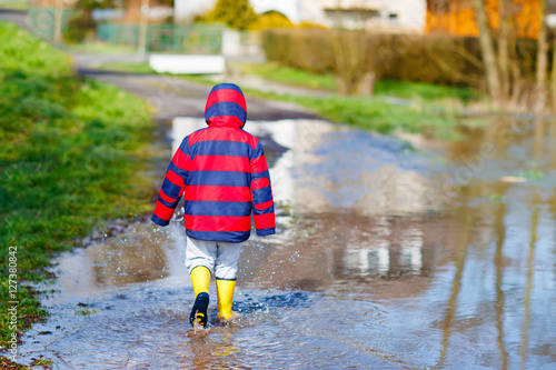 Little kid boy playing with paper ship by puddle