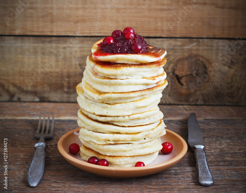 Stack of delicious pancakes with cranberries on plate and napkin  wooden background