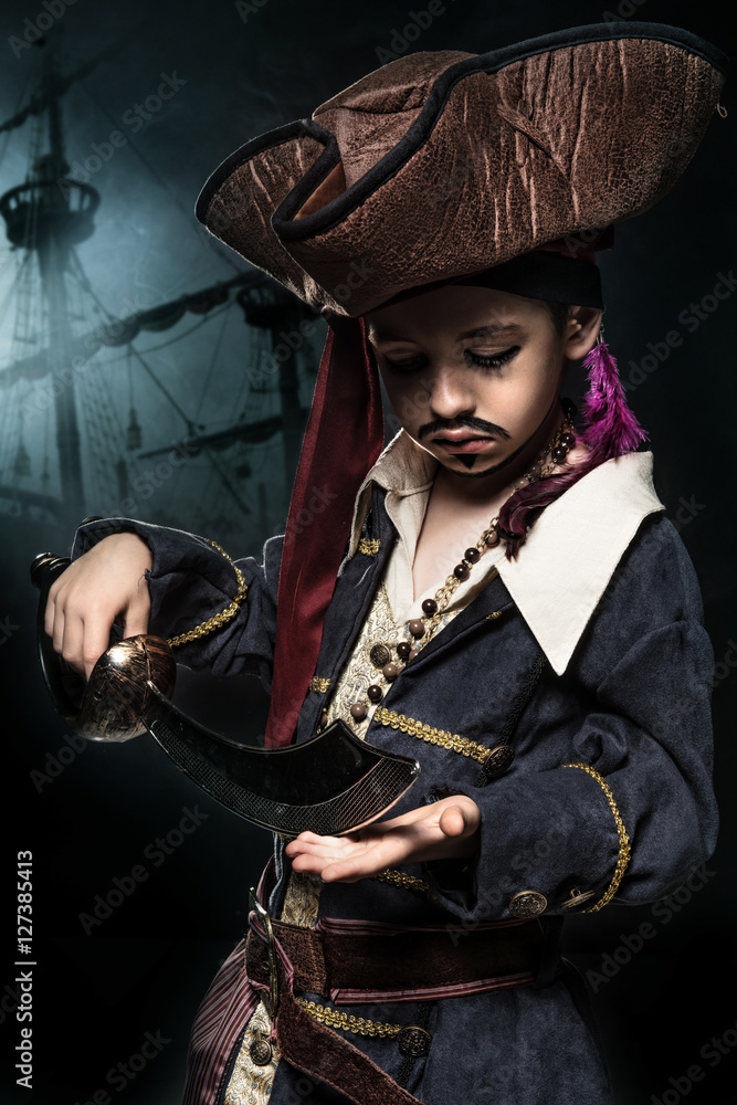 Fototapeta premium A angry young boy wearing a pirate costume. He stands on the background of the ship