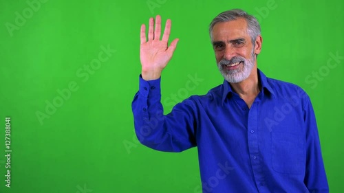 old senior man waves with hand - green screen - studio photo