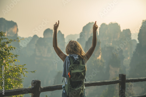 Young woman standing on top of the mountain with view over scenic area of Wulingyuan Park, raising her hands with thumbs up. Success conpect. photo