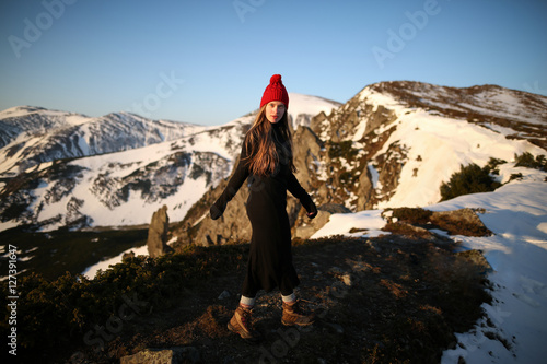 Young woman in a dress running in the mountains. Young girl in the mountains. Beautiful young smiling girl in her winter clothing. Woman on the background of snow winter and mounts