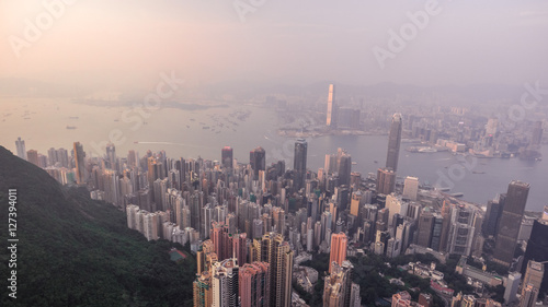 Beautiful aerial shot of many high skyscrapers covered with sunset fog or haze in Hong Kong, China. Top view of Victoria Harbour from Victoria Peak at sunset. City skyline. © drdonut