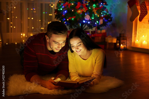 Young couple reading book in living room decorated for Christmas