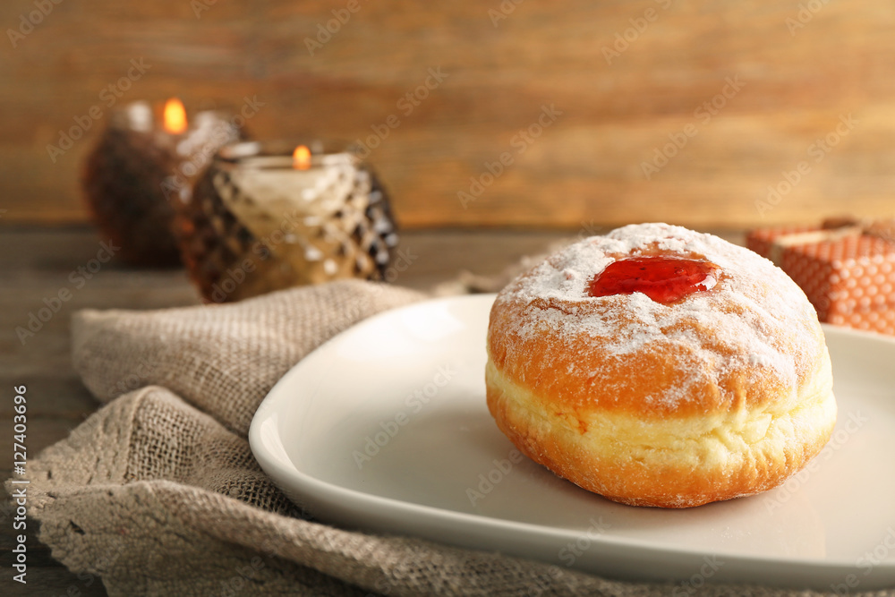 Plate with tasty donut on blurred wooden background, close up. Hanukkah celebration concept