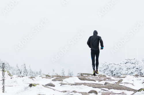 runner in black warm sportswear running in wind and fog on the high mountain trail in the winter
