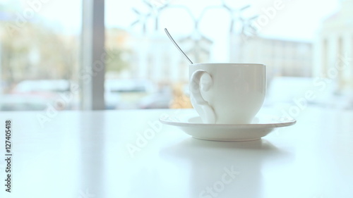 White cup on the table in coffee against a background window.