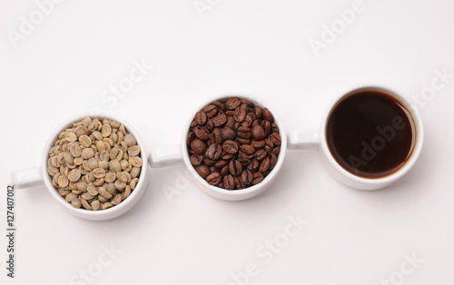 Three white cups with different stages of coffee: green and roasted beans and ready drink