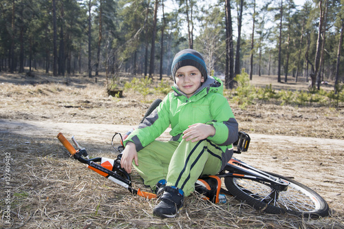 Happy baby funny little boy sitting with his bicycle in a pine f