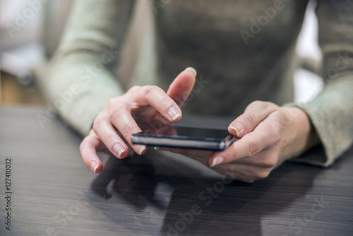 Woman holding a smartphone on the wooden table. Close-up hands 
