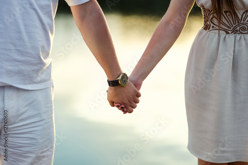 young couple holding hands on the shore of the river, hands close-up, love, feelings, sunset on the river