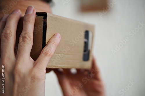 Male hands holding a cardboard goggles on the face as a symbol of modern digital life and symbol of a  tool used for watching movies and playing games in virtual reality 