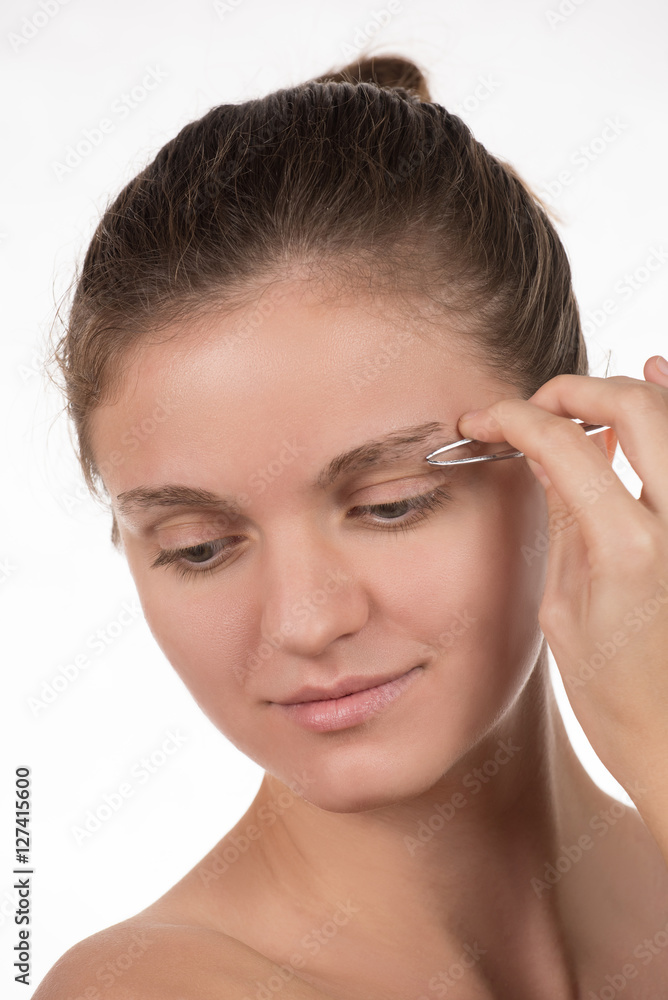 Young girl pulls out her eyebrows with tweezers metal on a white Young girl pulls out her eyebrows with tweezers metal on a white