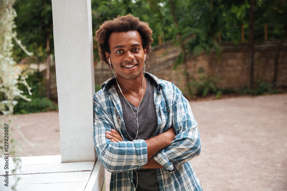 Fototapeta premium Smiling african man in earphones standing with arms crossed