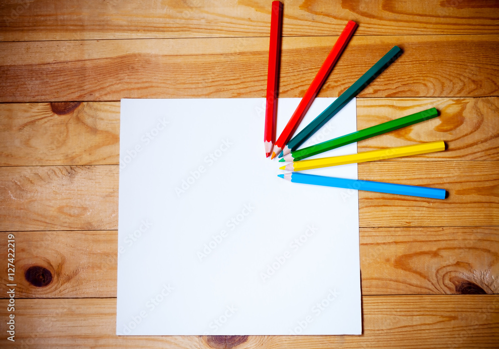 Blank paper and colorful pencils on the wooden background. View from above Blank paper and colorful pencils on the wooden background. View from above