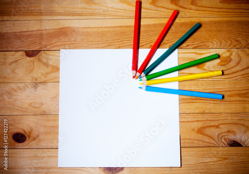 Blank paper and colorful pencils on the wooden background. View from above