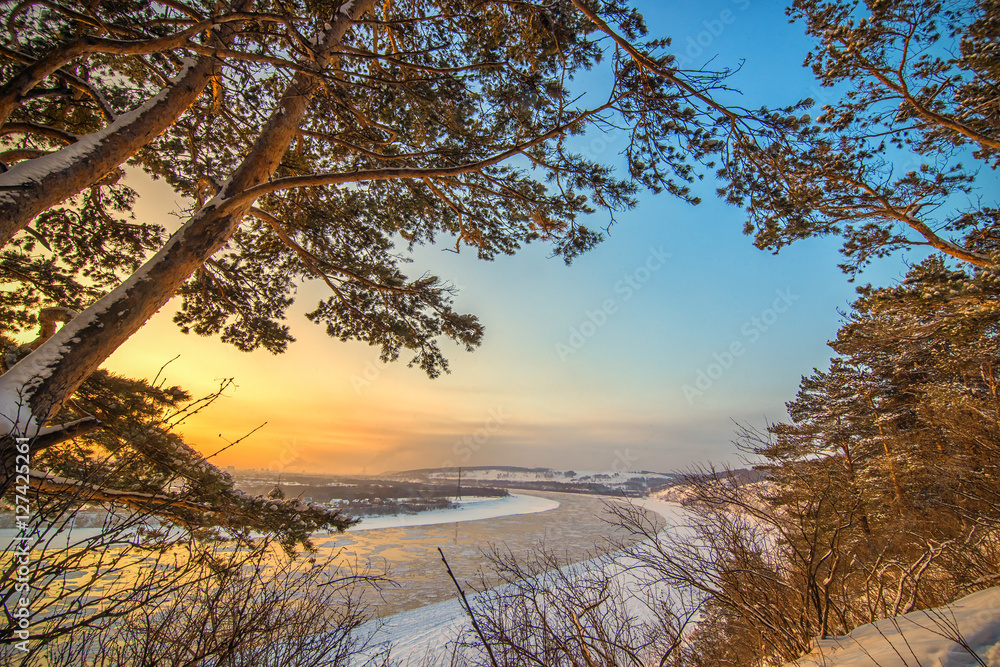 Landscape with sunset on frozen river and forest