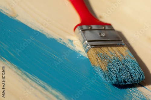 Red paintbrush painting wooden furniture in blue color, close up