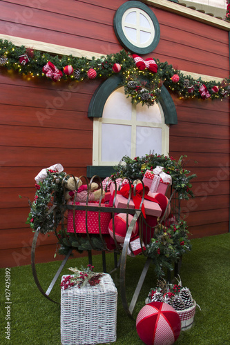 Fototapeta Naklejka Na Ścianę i Meble -  Christmas gifts inside sleigh, with flowers and decorated tree.
