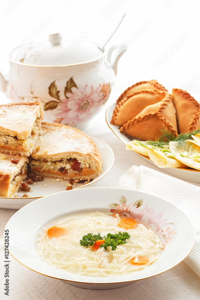 Traditional Tatar holiday table. Tokmach - noodle soup with chicken. Triangles - meat pies and sweet cake.