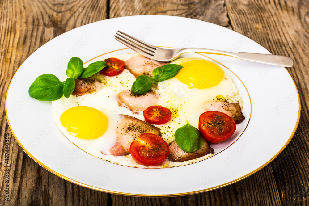 Fried eggs with bacon and vegetables on a white plate Fried eggs with bacon and vegetables on a white plate