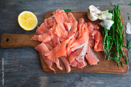 Fresh raw salmon slices with rosemary, garlic, lemon, pink and black on kitchen board. Top view. Selective focus.