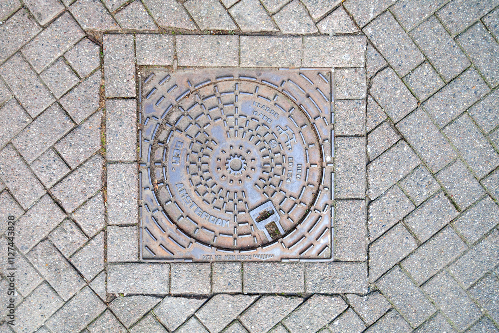 Manhole cover on pavement with patterns, Amsterdam