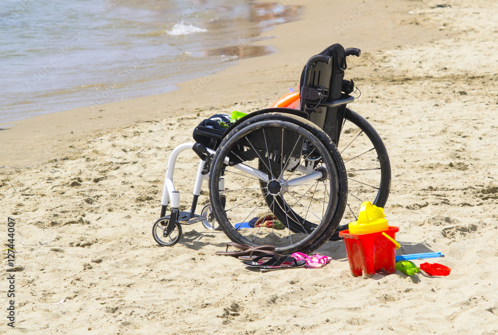 Foto Stock sedia a rotelle di un bambino sulla spiaggia | Adobe Stock