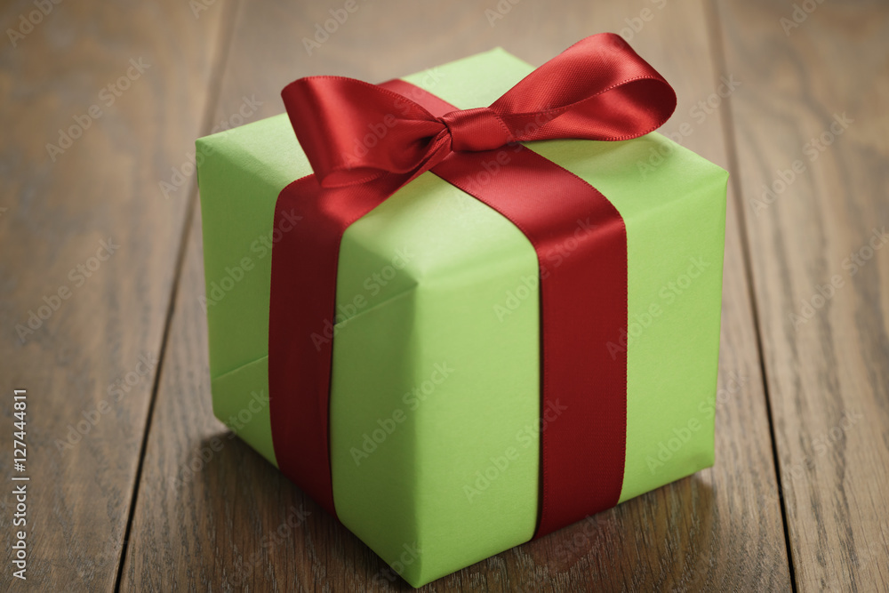 Obraz premium simple green paper gift box with red ribbon bow on oak table