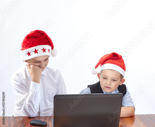 The boys in caps of Santa Claus looking at a laptop