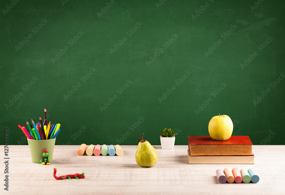 School items on desk with empty chalkboard School items on desk with empty chalkboard