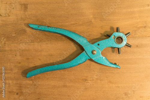 Leather Hole Punch Tool on wooden background - hole punch for leather goods Old blue Multiple revolving diameters puncher.