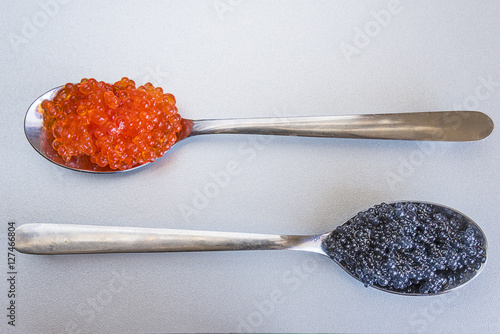 Luxurious meals: spoon with black caviar and spoon with salmon roe on snow background