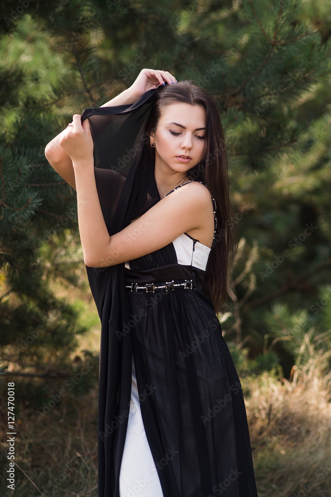 Graceful charming brunette model posing in black dress in coniferous park Graceful charming brunette model posing in black dress in coniferous park
