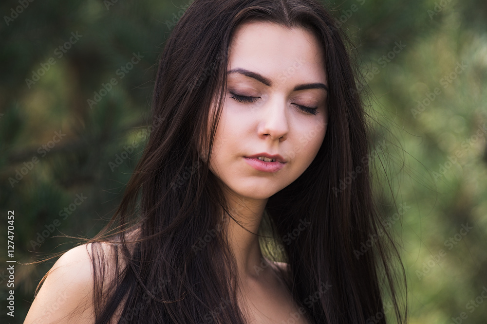 Fototapeta premium Graceful charming brunette model posing in black dress in coniferous park